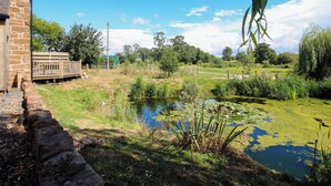 A stone building with a wooden deck, a pond with lily pads, and a fenced area with trees and grass. - The Old Mill (Telford)