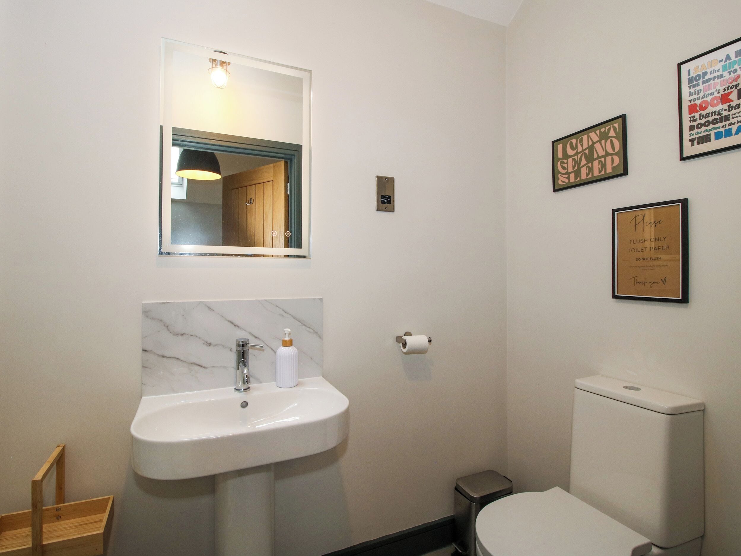 A bathroom with a white sink, a mirror, a toilet, and a trash bin.