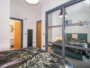 Ein Schlafzimmer mit Bett, Nachttisch, Lampe und einem Fenster mit Blick auf einen anderen Raum.