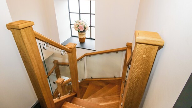 A wooden staircase with glass railings and a window with a flower vase. - The Old Mill (Telford)