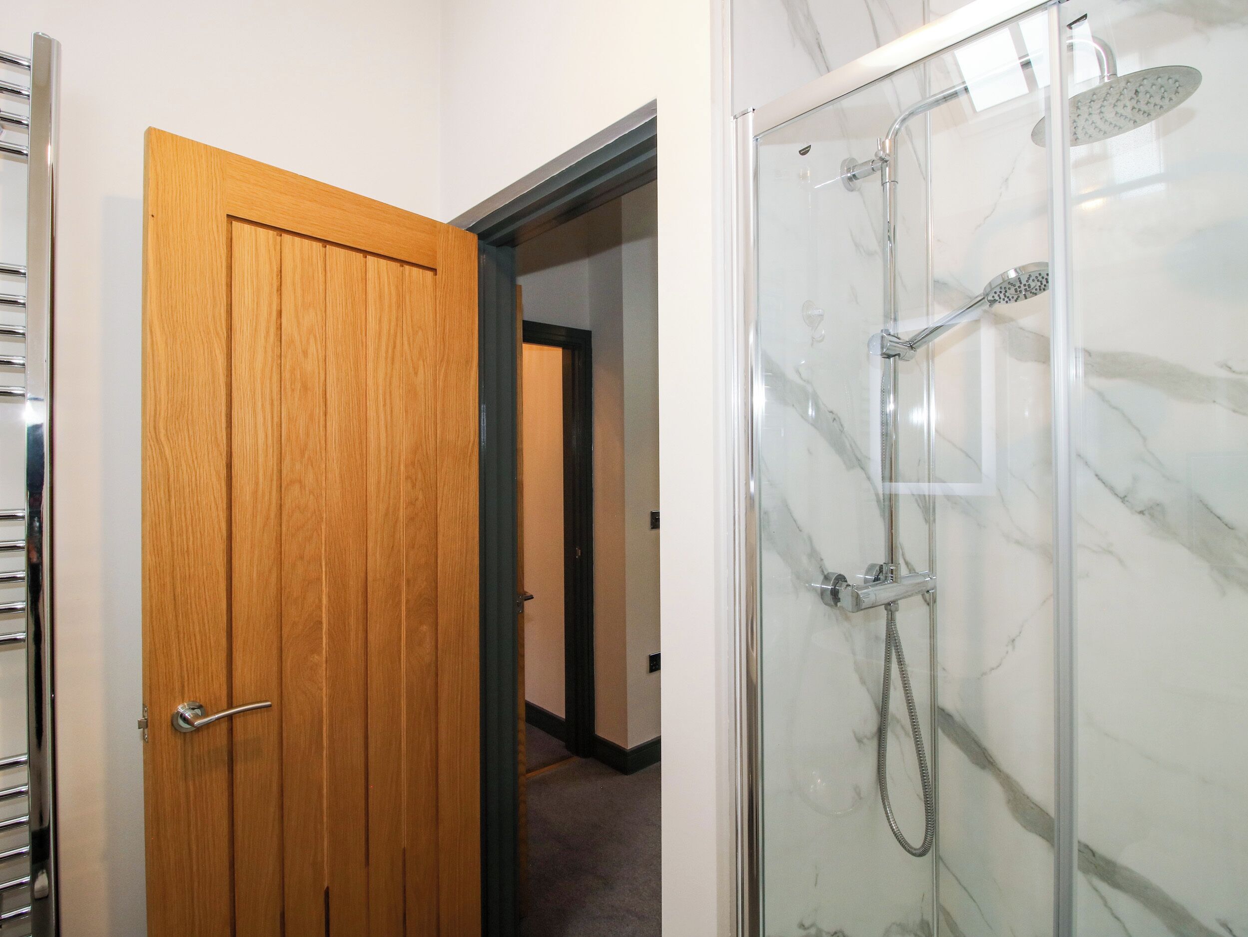 A bathroom with a glass-enclosed shower, a wooden door, and a towel rack.