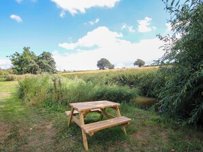 Ein Picknicktisch in einer grünen Wiese, im Hintergrund ein Teich und Bäume.