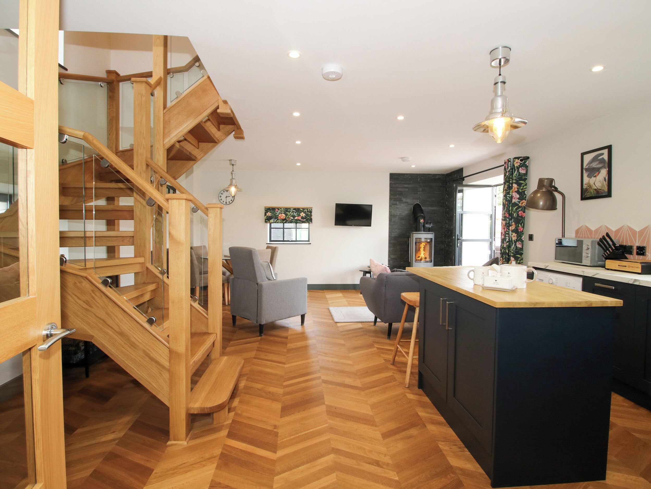 Une cuisine moderne avec un îlot central, un escalier en bois et une cheminée.