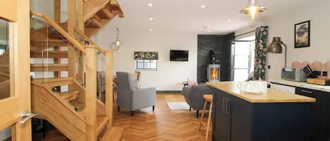 A modern kitchen with a central island, wooden staircase, and a fireplace.