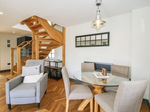 A modern living room with a glass-top dining table, grey upholstered chairs, a wooden staircase, and a pendant light. - The Old Mill (Telford)