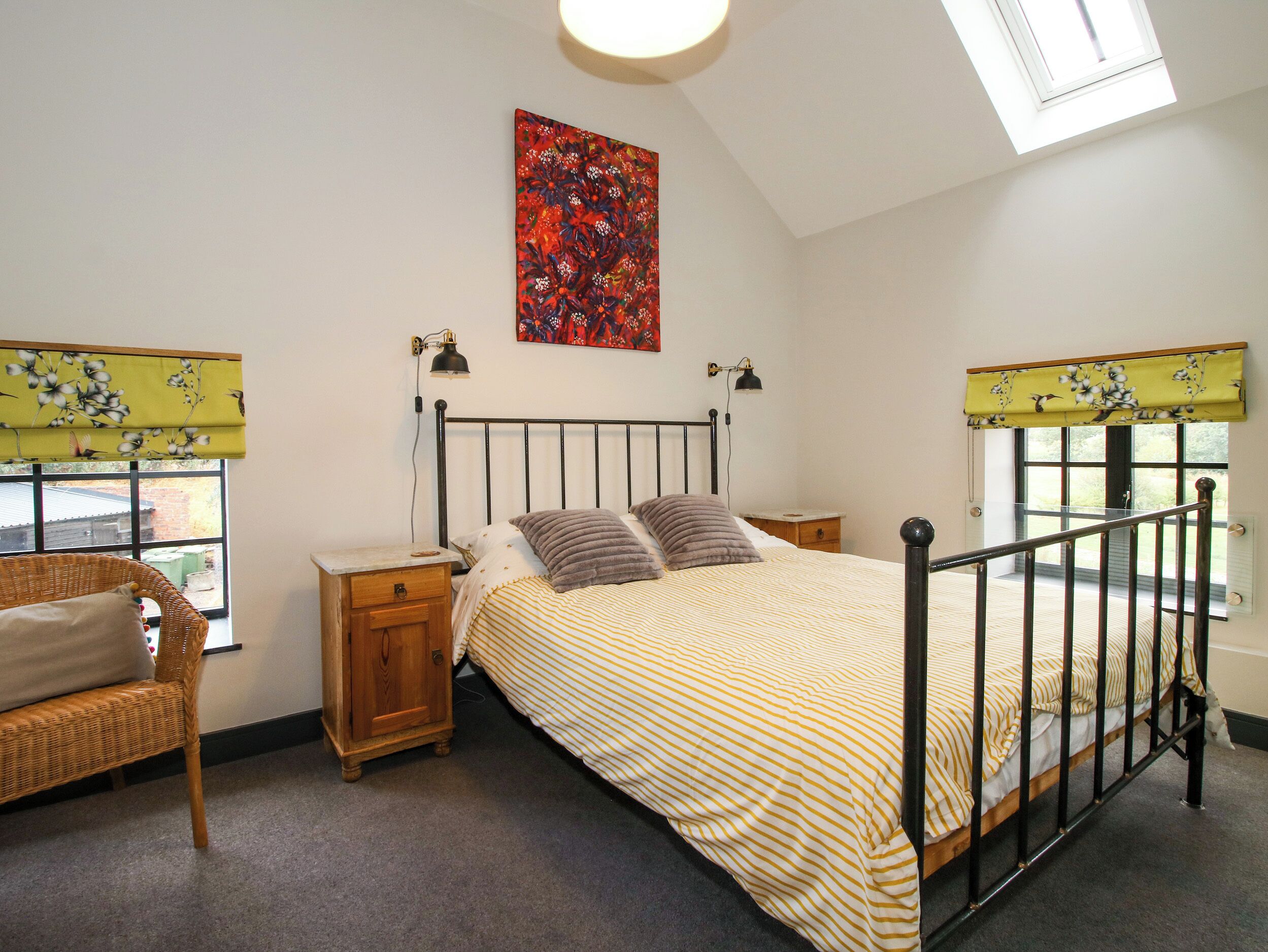 Une chambre à coucher comprenant un lit, deux tables de chevet, une commode, une fenêtre avec vue, un luminaire au plafond et une œuvre d’art accrochée au mur.