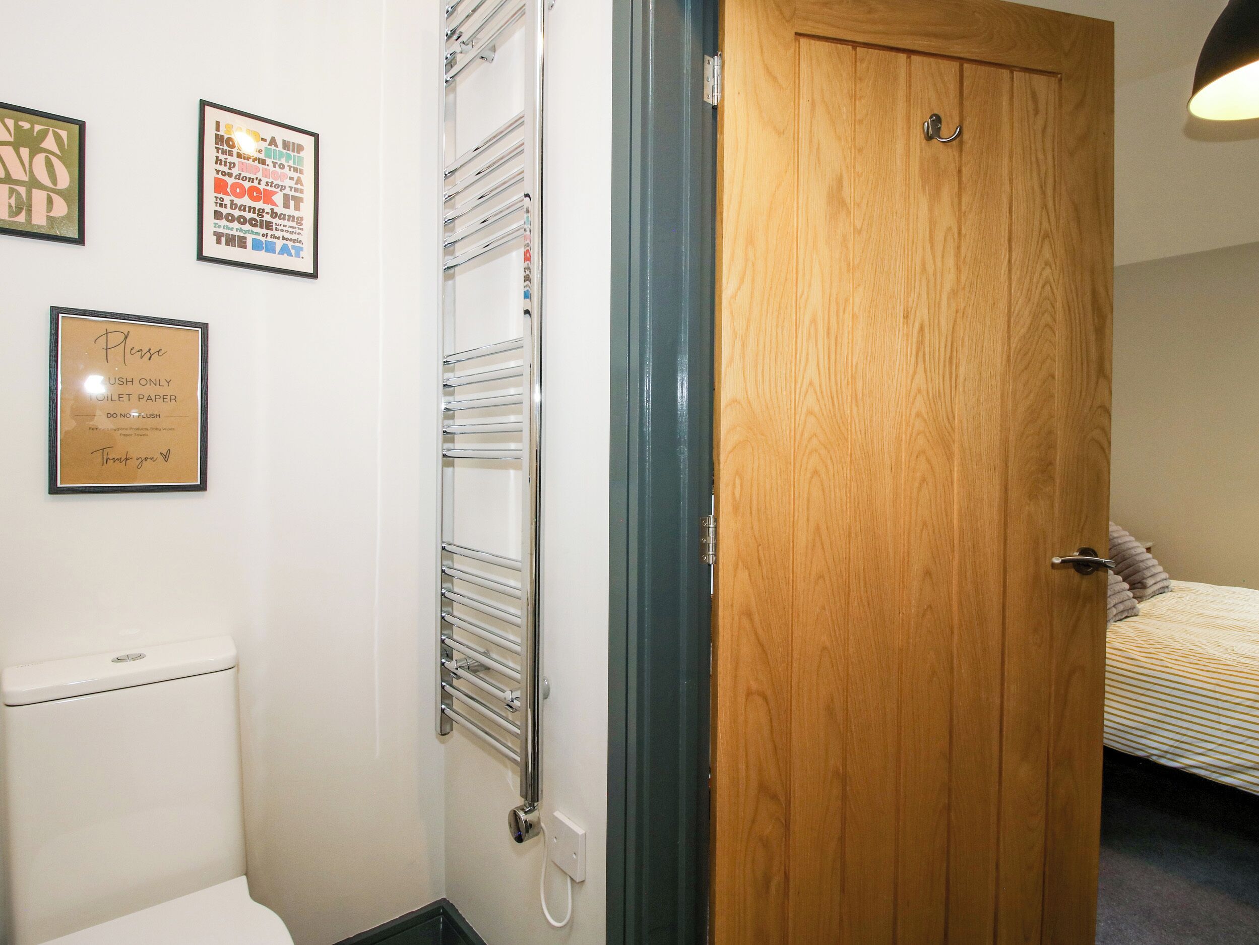 A bathroom with a toilet, a towel rack, and a wooden door leading to a bedroom.
