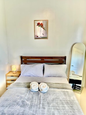 A neatly made bed with two rolled towels, a bedside lamp, and a framed picture on the wall.