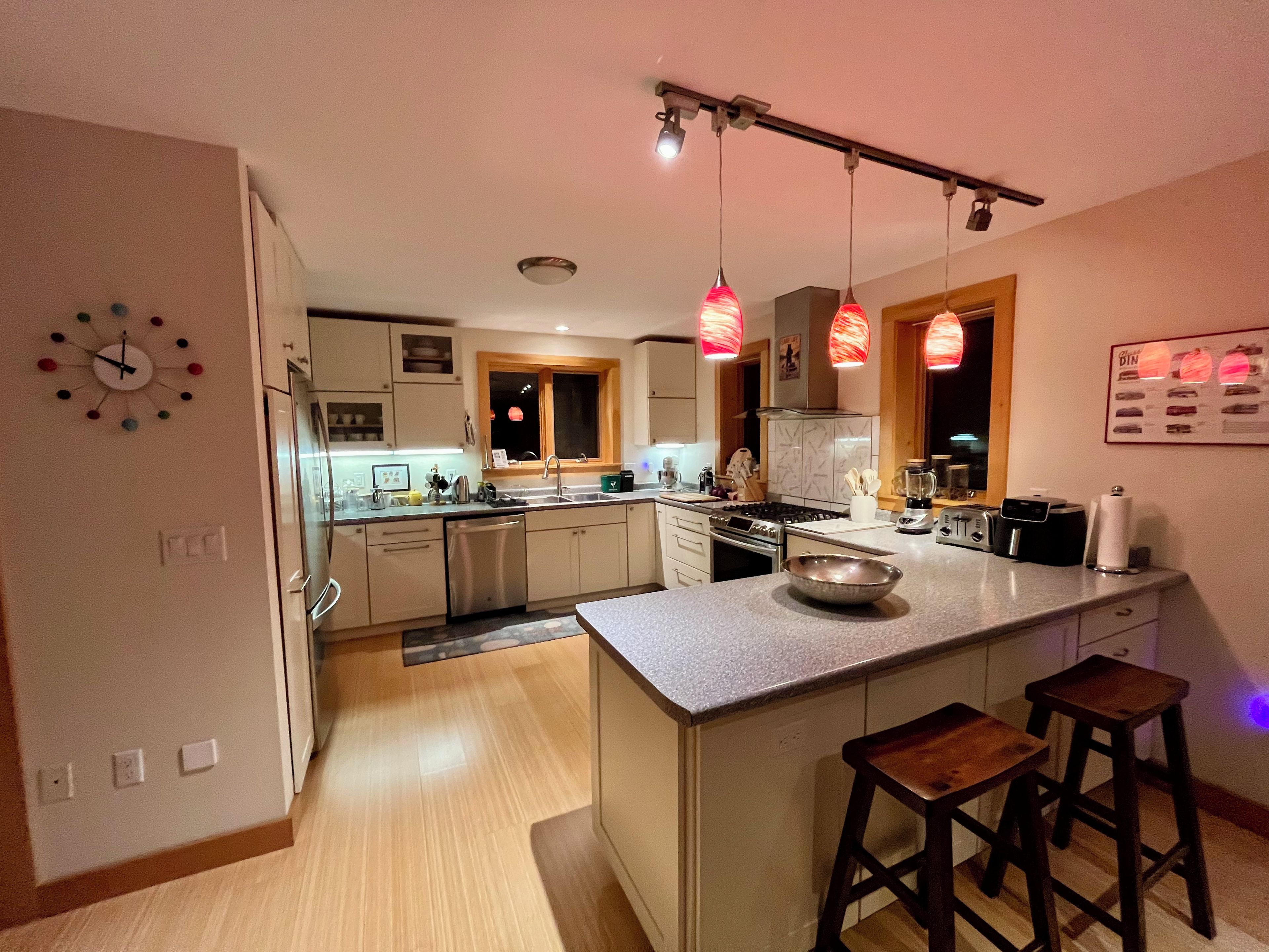 Een moderne keuken met een centraal eiland, hanglampen en een klok aan de muur.