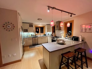 A modern kitchen with a central island, pendant lights, and a clock on the wall.