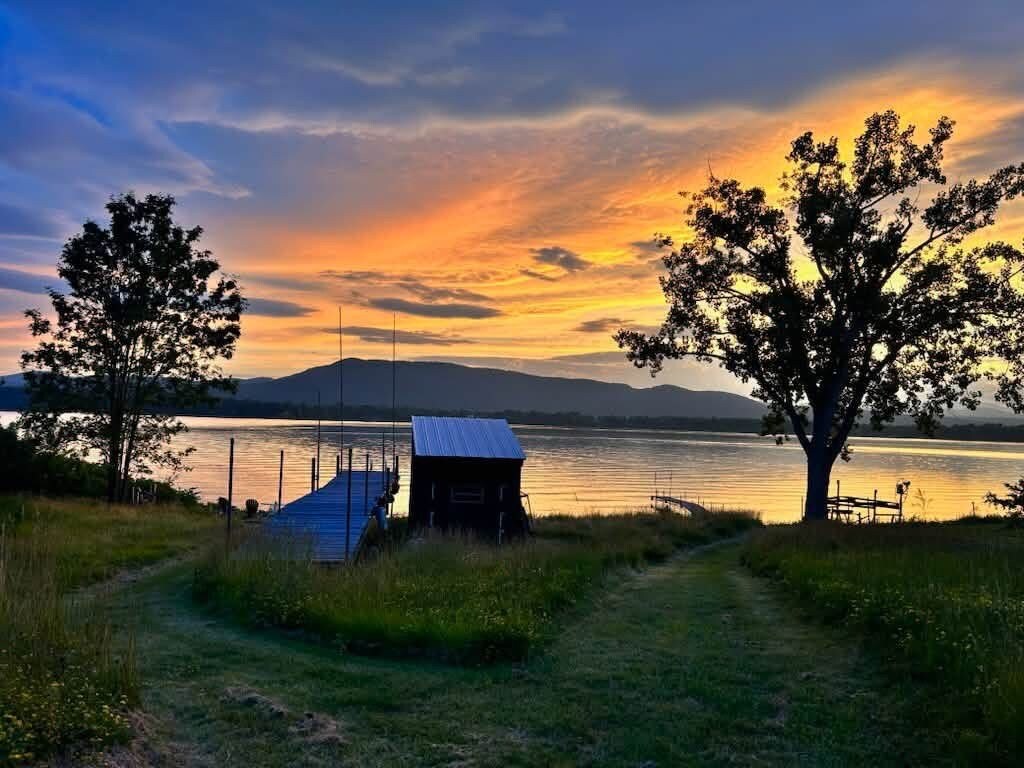 Escena a la vora d'un llac amb un moll, una cabana petita i arbres.