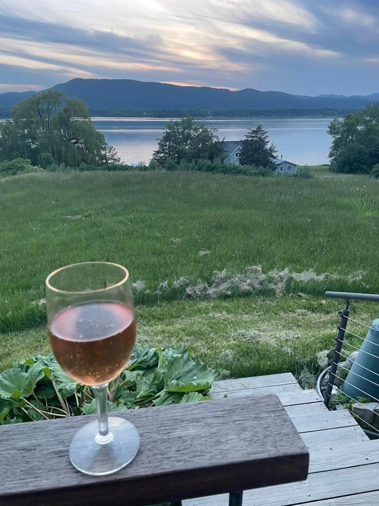 Et glas rødvin på et træbord med udsigt til en sø og bjerge i baggrunden.