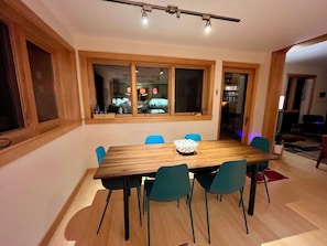 A dining area with a wooden table, blue chairs, and a window with a view of the kitchen.