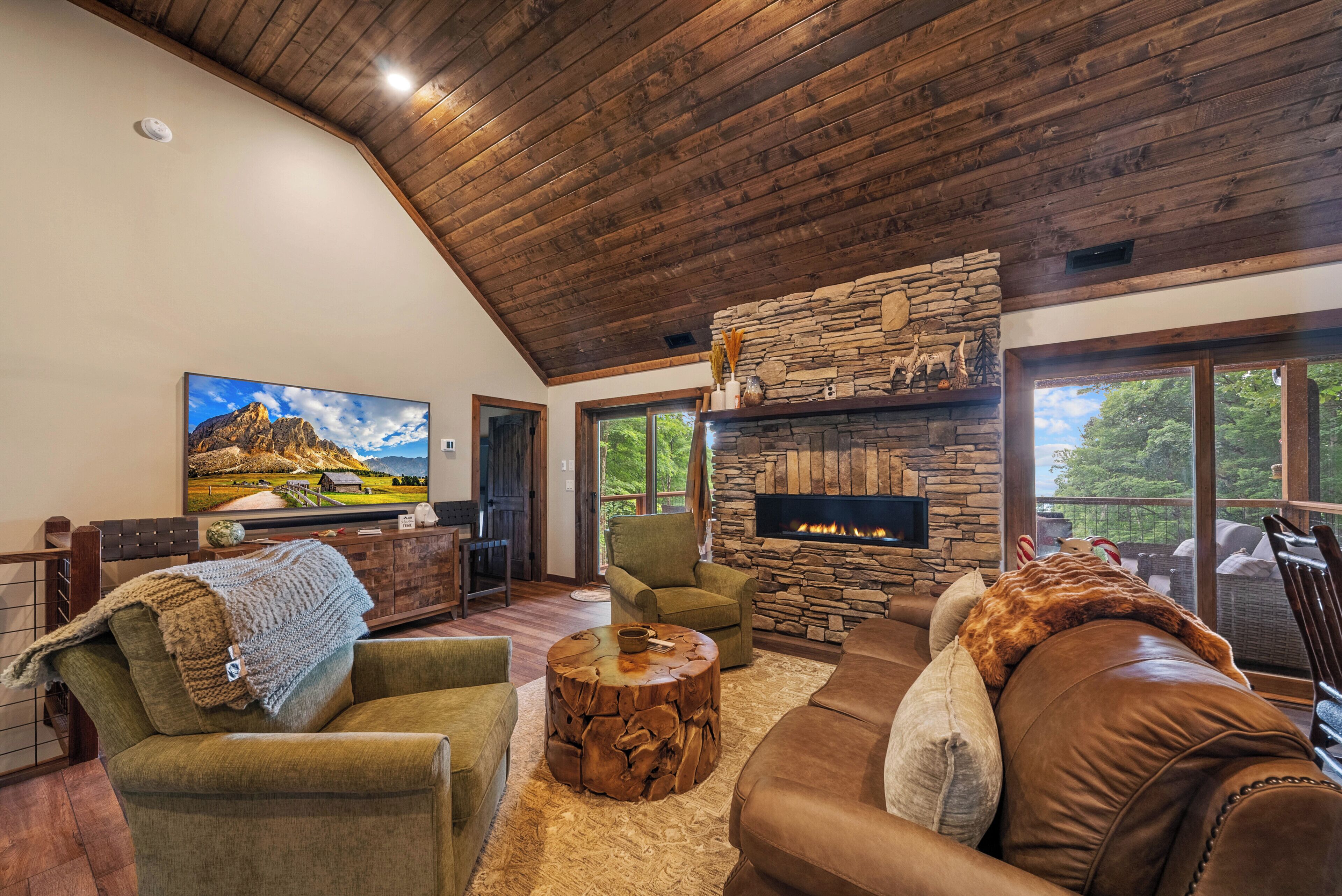 A spacious living room with a stone fireplace, comfortable seating, and a large window offering a view of the outdoors.
