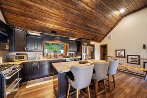 A kitchen with dark cabinets, a stainless steel refrigerator, a built-in oven, and a large island with bar stools. - Luxury Cabin with Hot Tub & Mountain Views (Zionville)