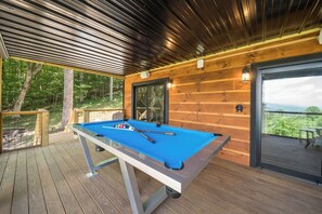 A pool table on a wooden deck with a covered area and a view of the outdoors. - Luxury Cabin with Hot Tub & Mountain Views (Zionville)