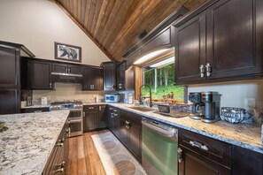Une cuisine moderne avec des meubles en bois foncé, des appareils électroménagers en acier inoxydable et une grande fenêtre donnant sur une forêt.