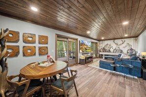 A modern interior with a wooden ceiling, a dining area with a round table and chairs, a sofa set, and a mural on the wall. - Luxury Cabin with Hot Tub & Mountain Views (Zionville)