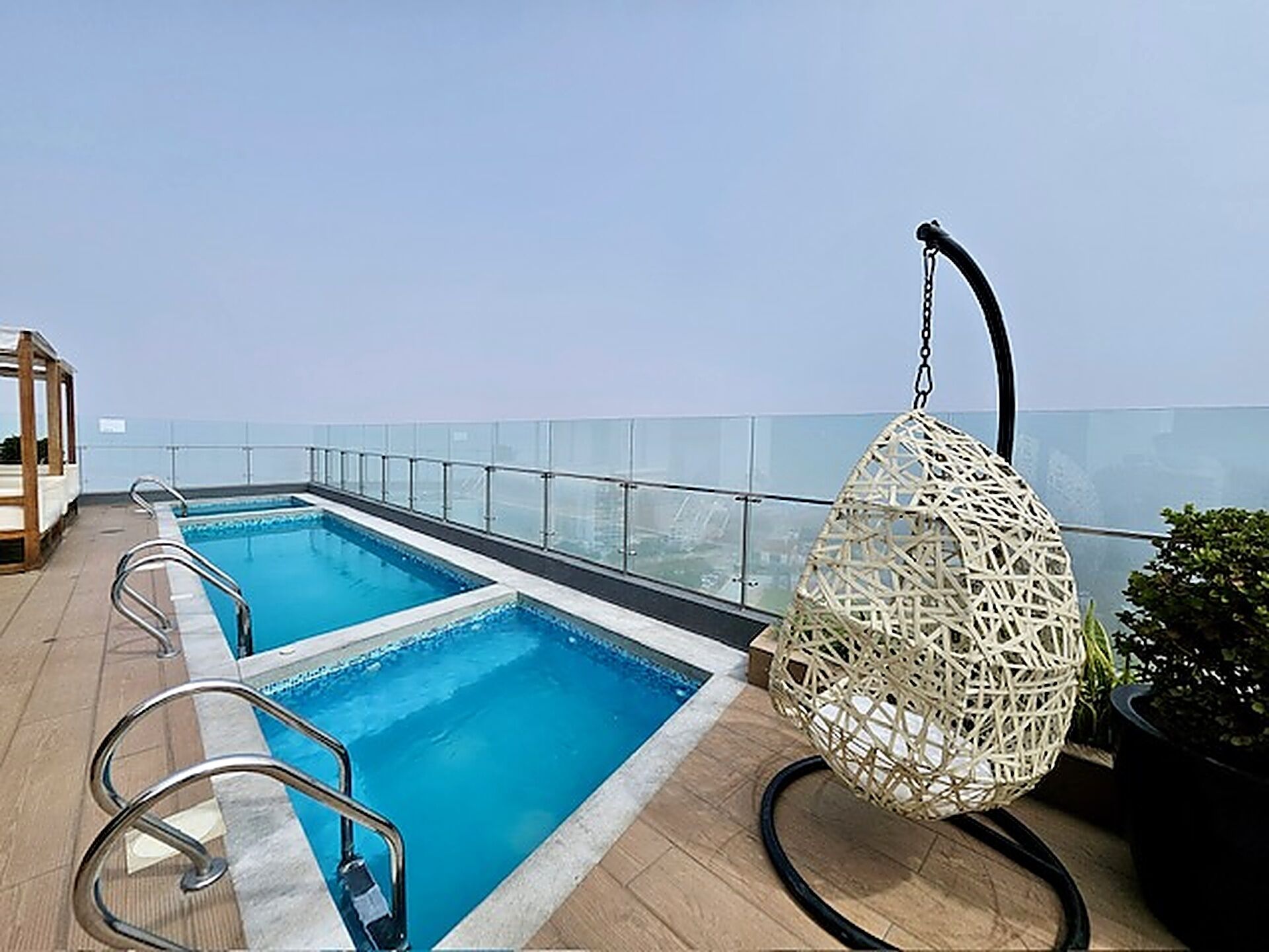 A rooftop pool with clear blue water, a glass balustrade, and a hanging wicker chair.