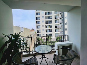 A balcony with a table and chairs, a potted plant, and a view of a multi-story building. - Barranco Luxe | A/C • Rooftop Pool & Hot Tub • Gym ⭐ (Barranco)