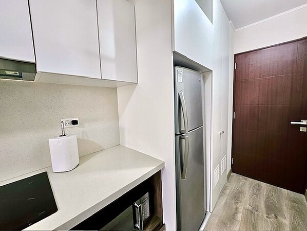 A compact kitchen with white cabinets, a stainless steel refrigerator, and a wooden door. - Barranco Luxe | A/C • Rooftop Pool & Hot Tub • Gym ⭐ (Barranco)