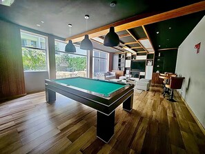 A modern living room with a pool table, wooden flooring, and a seating area with a sofa and chairs. - Barranco Luxe | A/C • Rooftop Pool & Hot Tub • Gym ⭐ (Barranco)