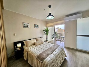 A bedroom with a bed, bedside table, lamp, and a view of a balcony. - Barranco Luxe | A/C • Rooftop Pool & Hot Tub • Gym ⭐ (Barranco)