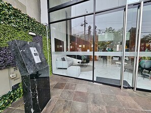 A reception area with a glass door, a marble reception desk, and a green hedge. - Barranco Luxe | A/C • Rooftop Pool & Hot Tub • Gym ⭐ (Barranco)