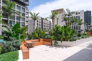 A modern outdoor area with a seating area, surrounded by lush greenery and tall buildings.