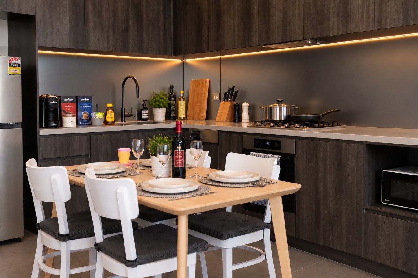 Een moderne keuken met een eethoek, voorzien van een kookplaat, spoelbak en diverse keukenapparaten.