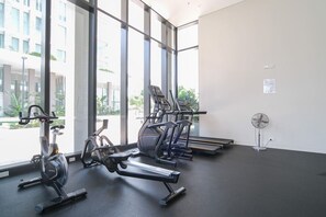 A gym with cardio equipment, large windows, and a standing fan.