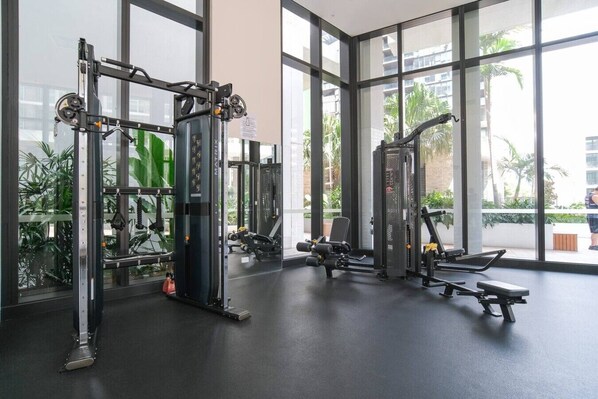 A gym with various exercise equipment, large windows, and a view of palm trees.