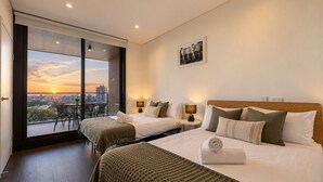 Et hotelværelse med to senge, en balkon med udsigt over byen og et lille bord med stole.