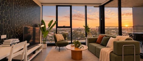 A modern living room with a large window, a sofa, a coffee table, and a bookshelf.