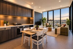 A modern kitchen with a dining area, a sofa, and a large window with a city view.