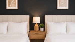 Habitación de hotel con dos camas, una mesita de noche con lámpara y una planta pequeña.