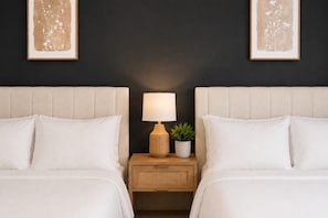 Habitación de hotel con dos camas, una mesita de noche con lámpara y una planta pequeña.