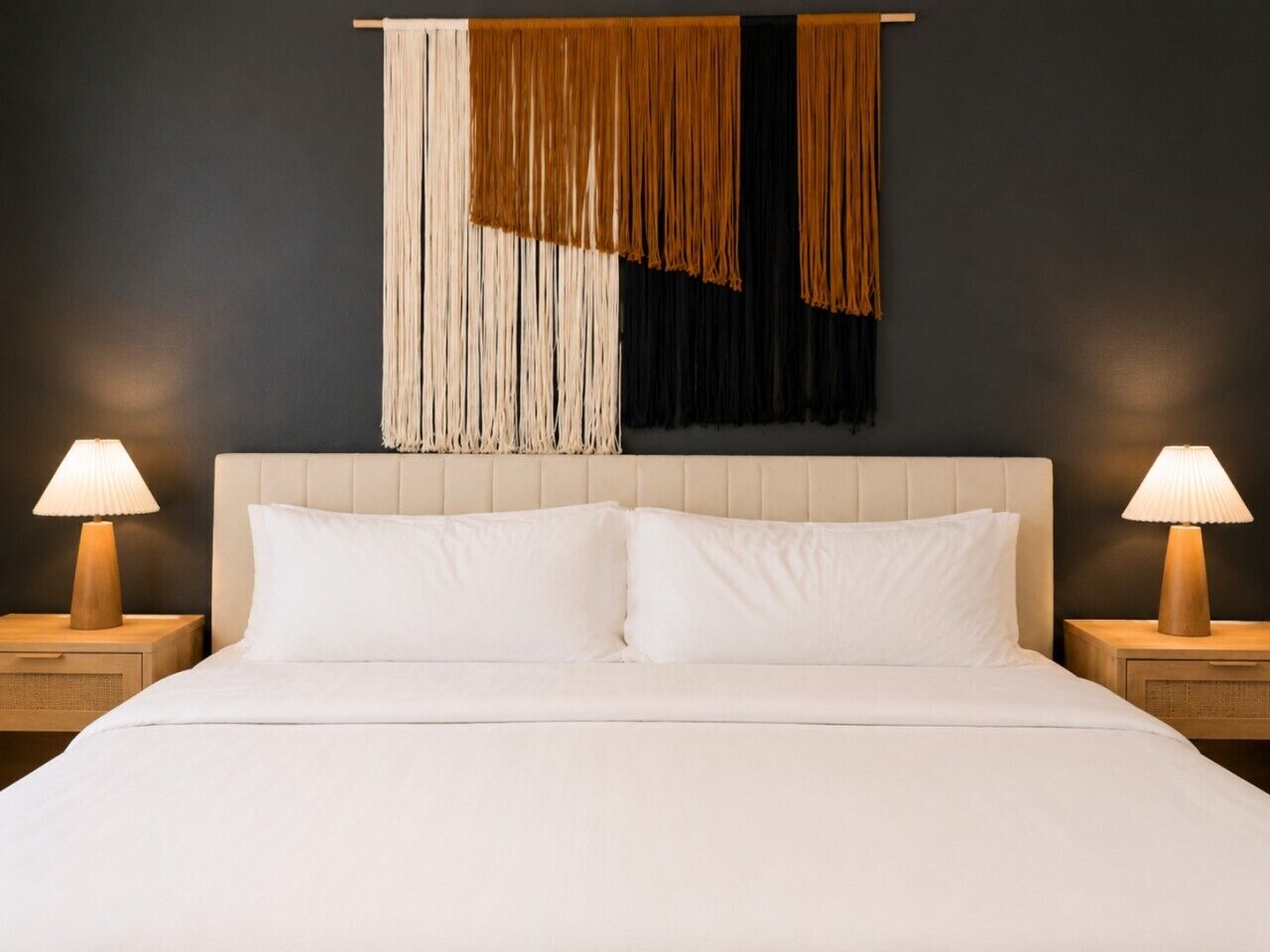 A hotel room with a large bed, two bedside tables with lamps, and a dark wall with a decorative hanging.
