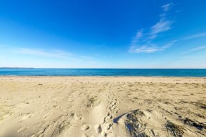 Ein Strand mit blauem Himmel, sandigem Ufer und Fußabdrücken.