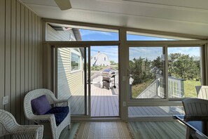 A room with a sliding glass door leading to an outdoor deck, a wicker chair, and a view of a house and trees. - Gorgeous Family Rental - Steps to Sagamore Beach (Sandwich)