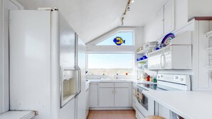 Cocina compacta con muebles blancos, microondas, estufa y ventana con vistas.