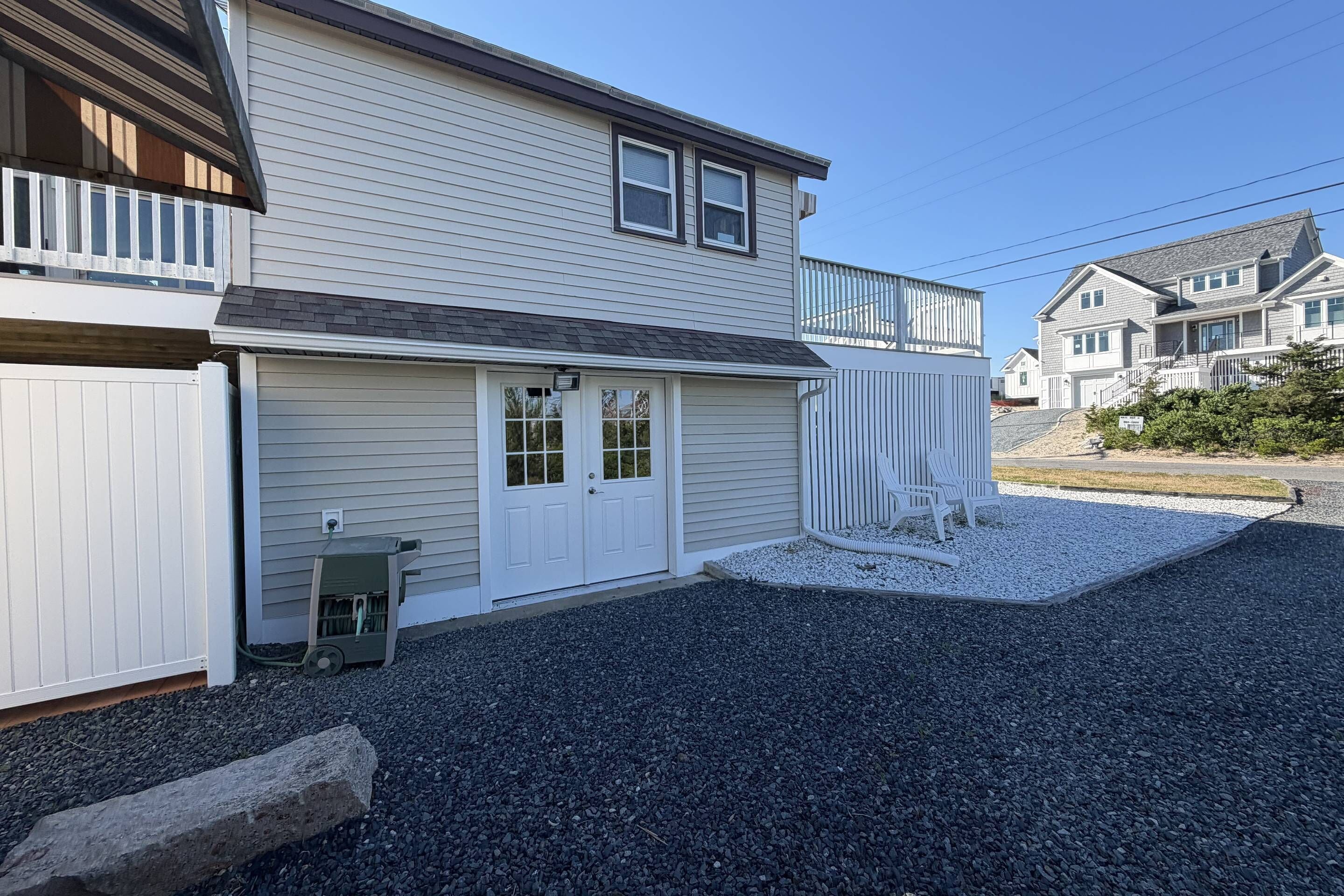 A two-story house with a garage, a gravel driveway, and a small garden area with a bench.