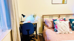 Ett sovrum med en säng, ett skrivbord med en stol, en lampa och en tavla som hänger på väggen.
