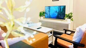 Ett vardagsrum med en platt-TV, två krukväxter, ett vitt soffbord och en soffa.