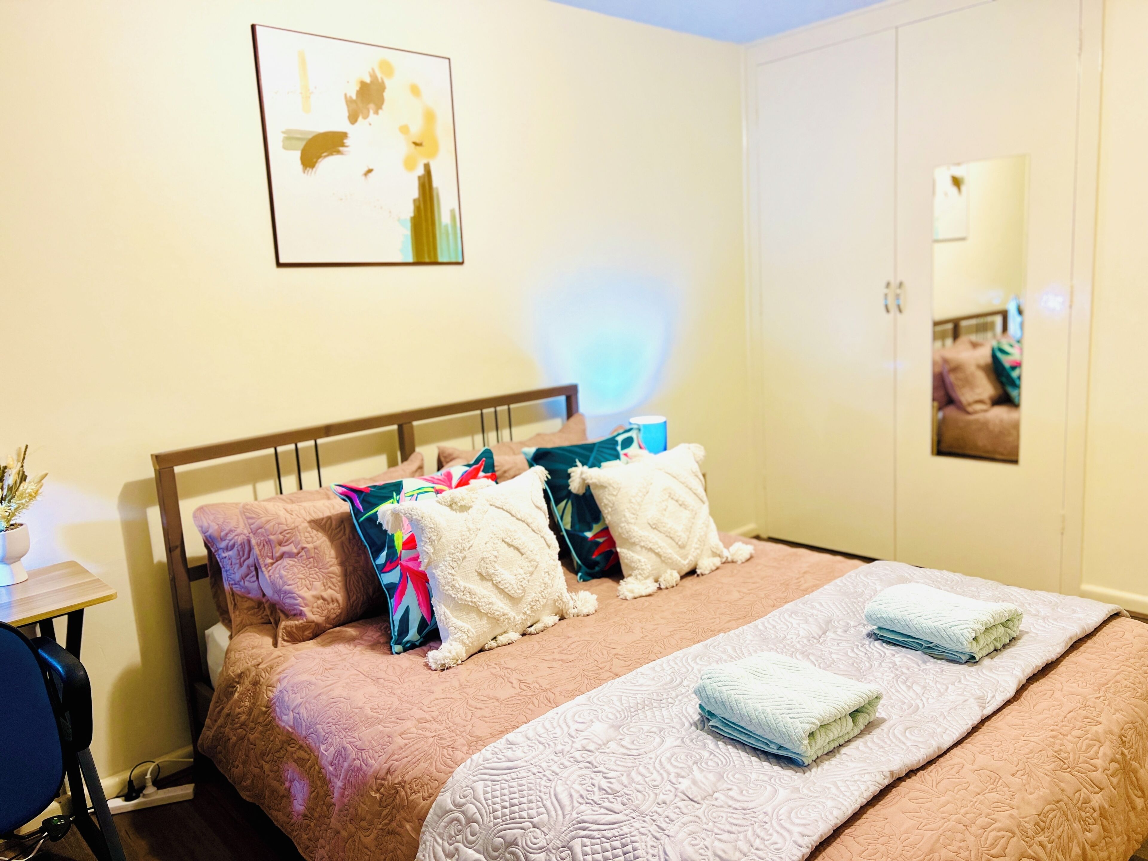 A hotel room with a bed, pillows, a bedside table, and a mirror.