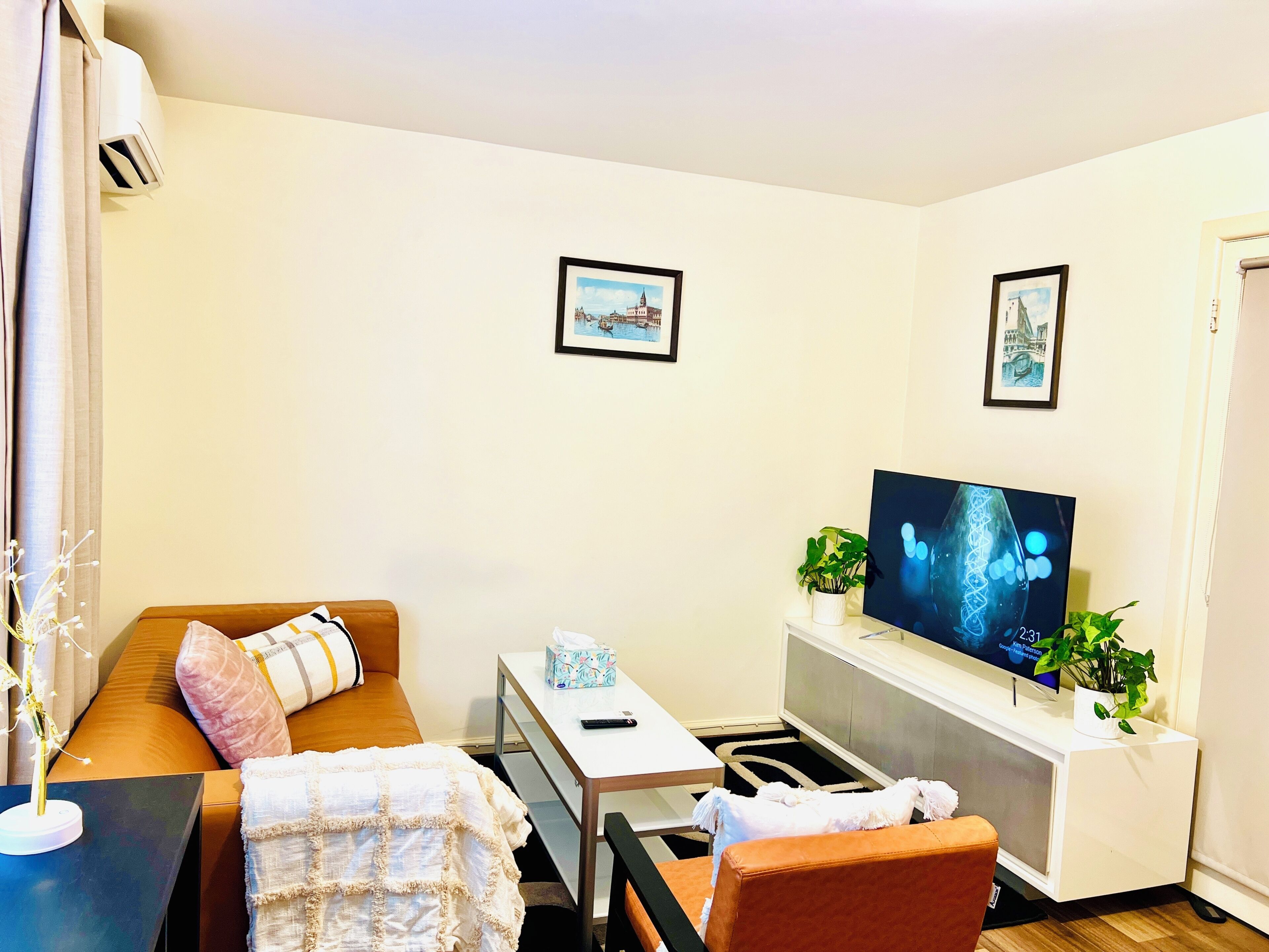 A living room with a sofa, a coffee table, a TV, and two framed pictures on the wall.