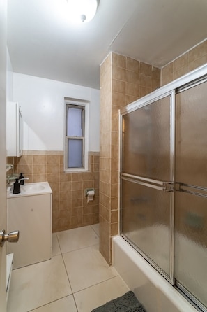 A bathroom with a shower, a sink, and a window. - Hells Kitchen 3BR, Walk to Times Square, Broadway & The Vessel (New York)