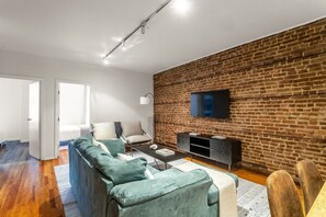 Ein modernes Wohnzimmer mit einem Ecksofa, einem Couchtisch und einem Flachbildfernseher an einer Ziegelwand.