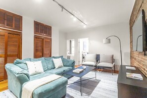 Un salon avec un canapé, une table basse et un fauteuil. Il y a un téléviseur accroché au mur et une porte qui donne sur une autre pièce.
