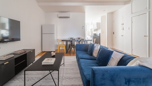 Ein modernes Wohnzimmer mit Flachbildfernseher, einer Couch, einem Couchtisch und einem Essbereich im Hintergrund.